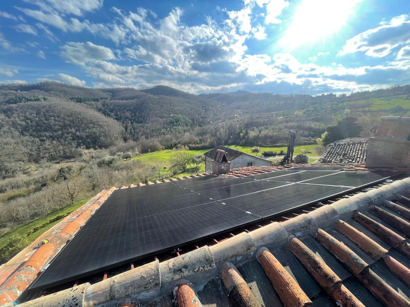 Installazione di pannelli fotovoltaici neri ad alta efficienza su un tetto in coppi di una casa immersa nel verde.