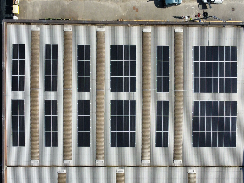 Vista aerea zenitale di un impianto fotovoltaico installato su un tetto industriale con pannelli monocristallini neri.