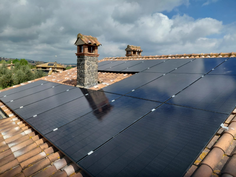 Primo piano di un impianto fotovoltaico con pannelli installati su un tetto in coppi di laterizio.