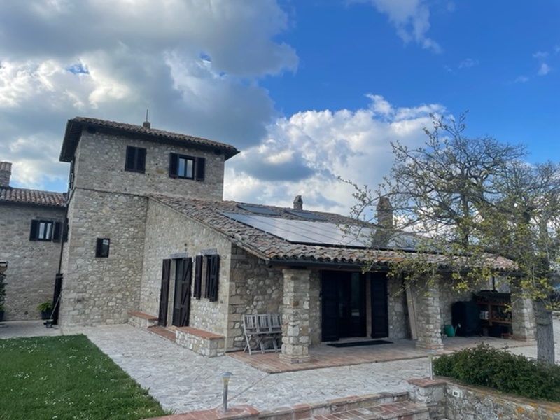 Facciata di un casale rustico in pietra a vista con un ampio impianto fotovoltaico posizionato sulla falda del tetto spiovente.